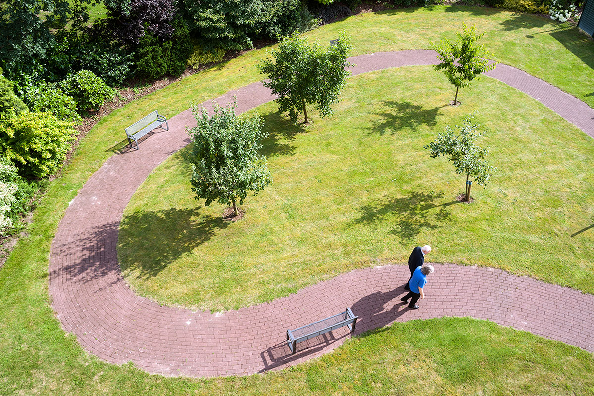 Bewohner:in spaziert mit Pflegeperson durch einen Park