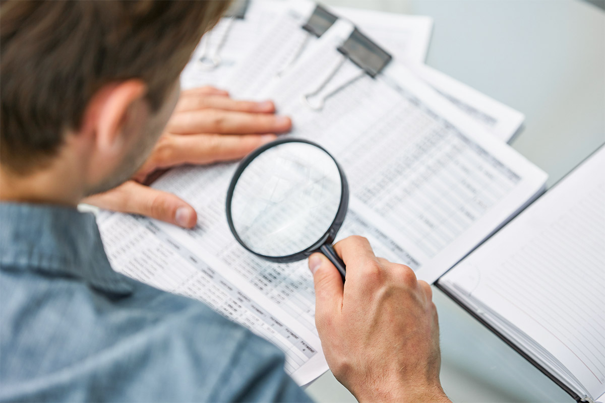 Geschäftsmann schaut mit Lupe auf Dokumente