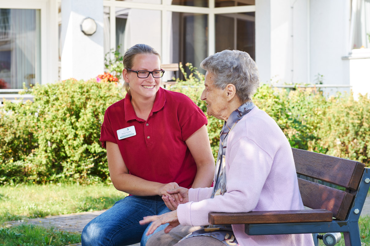 Seniorin mit Pflegerin im Park einer Alloheim Senioren-Residenz